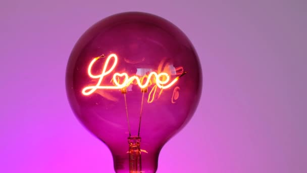 愛の概念。バレンタインデー。電球をオンにします。紫色の背景に碑文の愛と電球。愛と関係の象徴。バレンタインデー. — ストック動画