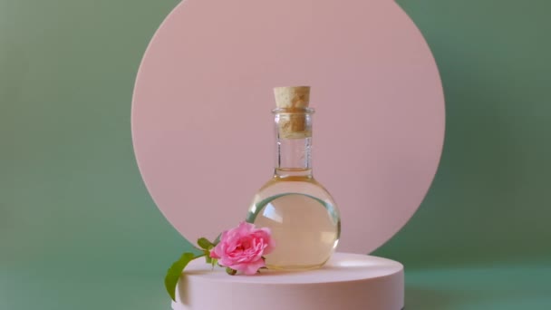Rozenolie.Aromatherapie en cosmetica.Biologische natuurlijke olie. Rozenolie in rozenblaadjes op een roze podium op een groene achtergrond.Biologische bio cosmetica — Stockvideo