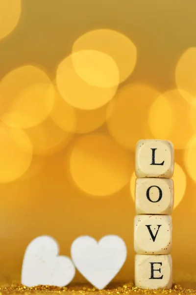 Amor y relación.Día de San Valentín. Inscripción amor hecho de letras de madera y corazones blancos sobre un fondo de brillo de oro con bokeh oro. — Foto de Stock