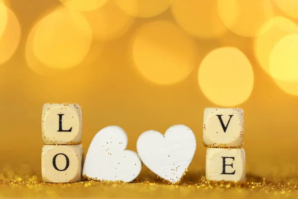 Amor y relación.Día de San Valentín. Amor de inscripción hecha de letras de madera y corazones blancos sobre un fondo de brillo de oro con bokeh oro. Fondo de San Valentín en tonos dorados. — Foto de Stock