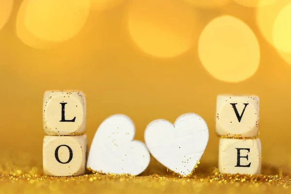 Valentines Day. Inscription love made of wooden letters and white hearts on a gold glitter background with gold bokeh. Valentines day background in gold tones. — Stock Photo, Image