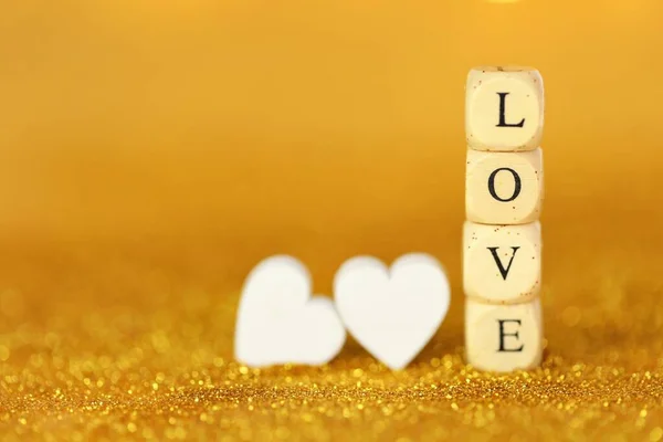 Amor e relacionamento.Dia dos Namorados. Inscrição amor feito de letras de madeira e corações brancos em um fundo brilho ouro com bokeh ouro. Dia dos namorados fundo em tons de ouro.Símbolo do amor — Fotografia de Stock
