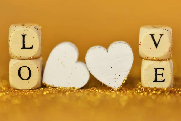Liefde en relatie.Valentijnsdag. Inscriptie liefde gemaakt van houten letters en witte harten op een gouden glitter achtergrond. Valentijnsdag achtergrond in gouden tinten. — Stockfoto
