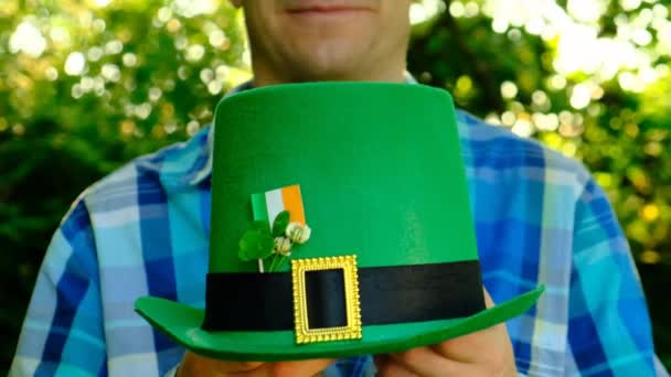 聖パトリックのお祝い晴れた春の庭で男の手に緑の帽子のクローズアップ4枚葉のクローバー。幸運を象徴するアイルランドの伝統的な春の休日 — ストック動画