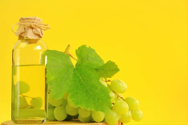 Масло виноградного насіння. Базова косметична олія для масажу та догляду за обличчям та тілом. пляшка і пучок зеленого винограду на жовтому фоні.Органічна олія білого винограду . — стокове фото