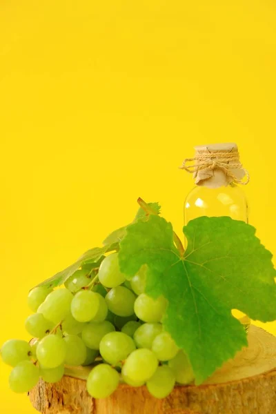 Huile de pépins de raisin Huile cosmétique de base pour massage et soin du visage et du corps. bouteille et bouquet de raisins verts sur fond jaune. — Photo