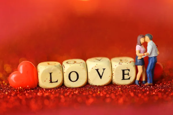 Valentijnsdag. Liefdessymbool. Verliefd paar figuurtjes, Inscriptie liefde gemaakt van houten letters op een rode glitter achtergrond — Stockfoto