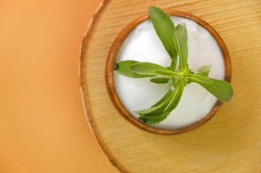  Stevia Rebaudiana turuncu arka planda. Turuncu arka planda kesilmiş tahta testereyle kristal stevia tozuyla ahşap bir fincanda Stevia dalı..
