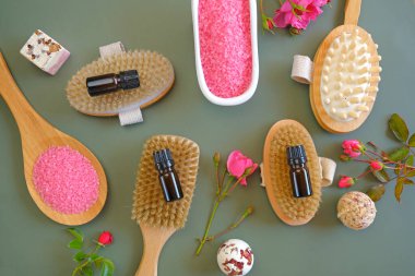 Rose oil and cosmetics salt with rose extract and body brushes on a green background.Aromatherapy and cosmetics. Glass bottles set ,rose flowers and pink cosmetics salt.