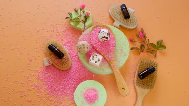 Rose oil, cosmetics salt and body brushes with natural bristles.Rose flowers and salt with rose extract on orange background.Organic rose oil.Organic bio cosmetics.Aromatherapy and cosmetics. — Stock video
