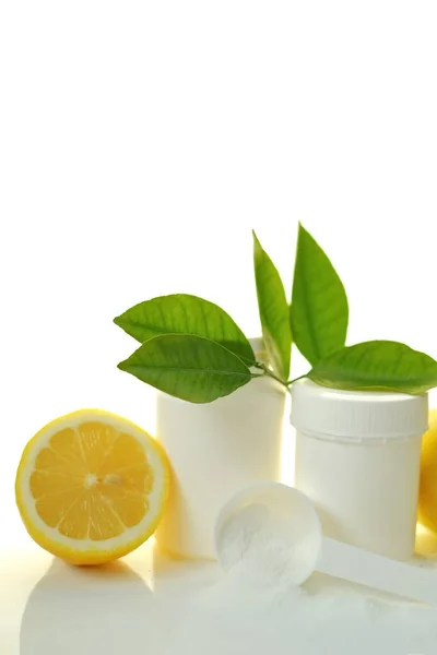 Poudre de vitamine C, cuillère blanche, pot blanc et citron dans une coupe aux feuilles vertes isolées sur fond blanc. — Photo