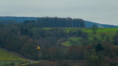 Helikopter geliyor. Sarı helikopter dağların ve tarlaların üzerinden gökyüzüne uçuyor. Ambulans tıbbi helikopteri