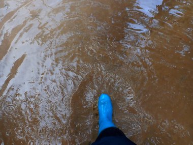 Bahar göleti. Su birikintisi yürüyüşü. Baharda çamurlu suda mavi lastik botlar. Suya basamaklar. Lastik botlar su birikintilerinde yürüyor. çamur ve su birikintileri. Hava ve doğa.