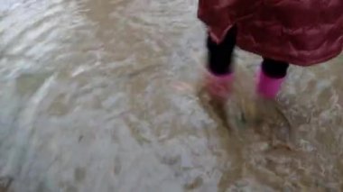 Bahar birikintisi. Pembe lastik çizmeli kız su birikintilerinde yürüyor. çamur ve su birikintileri. Hava ve doğa.