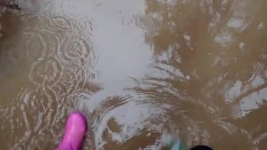 Su birikintisi. Su birikintisi. Ayaklar mavi ve pembe lastik botlar. Bahar çamurlu suda. Lastik botlar su birikintilerinde yürüyor. Çamur ve su birikintileri. Hava ve doğa.