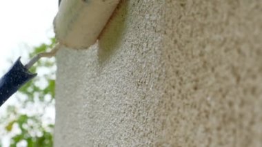 Duvar boyası. Paten evin duvarlarını bej rengine boyuyor. Evin rengini bej rengine boyuyor. Dışarıda tadilat var. İnşaat ve yenileme. Duvarı silindirle boyamak.