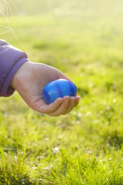 Paskalya Yumurtası Avı. Paskalya, güneşin altındaki bahar bahçesinde bir çocuğun elinde yumurta boyadı. Renkli yumurtalar. Paskalya bayramı geleneği. Dini bayram.