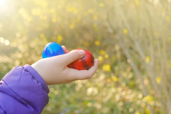 Пасхальные яйца в детской руке в цветущем весеннем саду на солнце. Красочные яйца. Традиционный пасхальный праздник. — стоковое фото