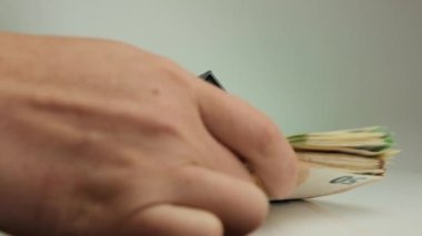 Ev satın alma, emlak alım ve satımı. El bir yığın banknot koyar ve evi alır. Emlak piyasası. Beyaz dekoratif evler ve yeşil arka plandaki avro banknotları.