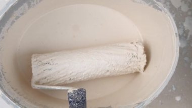 Duvar boyası ve yenileme. Paten ve boya. Bej boyalı bir kovada inşaat rulosu. Bej tonlarda ev boyası..