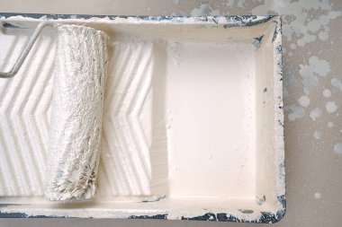 Duvar boyası ve yenileme. Paten ve boya. İçinde boya olan bir konteynırda rulo. Bej renkte ev boyası..