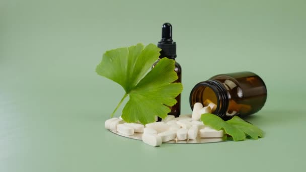 Ginkgo biloba leaf ,white tablets and liquid ginkgo biloba extract in brown glass jars on green background.Preparations with ginkgo biloba extract — Stock Video