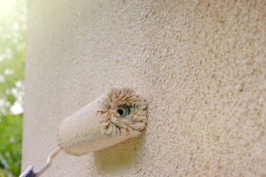 Evin duvarlarını bej rengiyle boyayan tekerlekli paten. Bej bir duvarda boyanmış bir bina silindiri. İnşaat ve yenileme işleri..