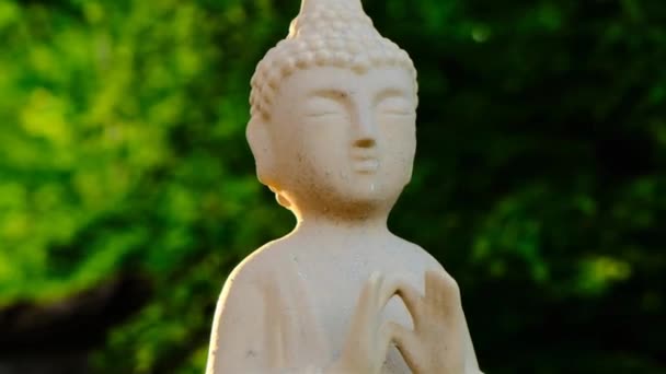 Buddha-Statue auf grünem Gartenhintergrund in den Sonnenstrahlen. Buddhismus religiöser Hintergrund. Ruhe, Ausgeglichenheit und Harmonie. Buddhismus-Symbol. Meditation und Entspannung — Stockvideo