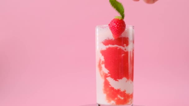 Cocktail à la fraise.Cocktails d'été et buves.main met de la menthe poivrée dans un verre à cocktail. cocktail et crème dans un gobelet aux fraises et brins de menthe sur fond rose.. — Video
