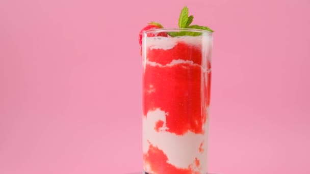 Jordgubbscocktail med kräm.Rosa cocktail och grädde i transparent glasbägare med jordgubbar och myntkvistar på rosa bakgrund. Rotation.Sommarcocktails och drinkar.Bär smoothies — Stockvideo