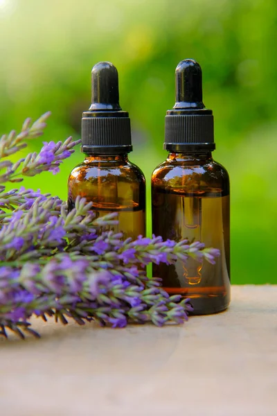 Lavendelöl und Lavendelzweige auf verschwommenem grünem Hintergrund. Kosmetisches Basisöl zur Massage und Pflege von Gesicht und Körper. Lavendel ätherisches Öl Glasflaschen. — Stockfoto