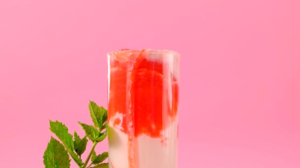 Jahodové koktejly. Pijte z letních bobulí a mlíka.Růžový koktejl a smetana v průhledném skleněném poháru s jahodami a sprigy máty na růžovém pozadí.Letní koktejly a nápoje. — Stock video