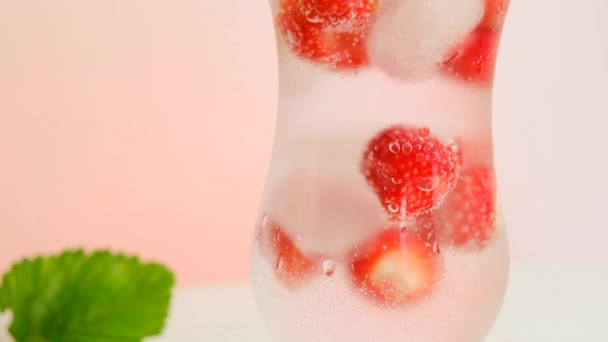 Agua de fresa con hielo y fresas en una copa de vidrio y fresas maduras con hojas — Vídeos de Stock