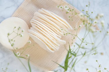 Sıfır atık. Yeniden kullanılabilir kumaş küreleri. Organik pamuk doku kozmetik süngerler ve gri mermer arka planda beyaz çingene çiçekleri. Çevre dostu doğal kozmetik ürünler. makul tüketim