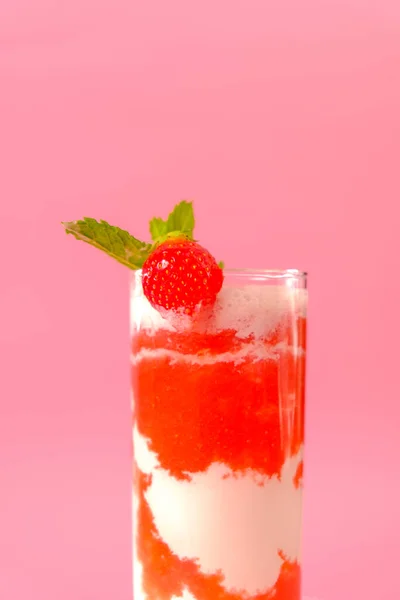 Aardbeiencocktail met crème.Berry smoothies. Roze cocktail en crème in een glazen beker met aardbeien en munttakjes op een roze achtergrond. — Stockfoto