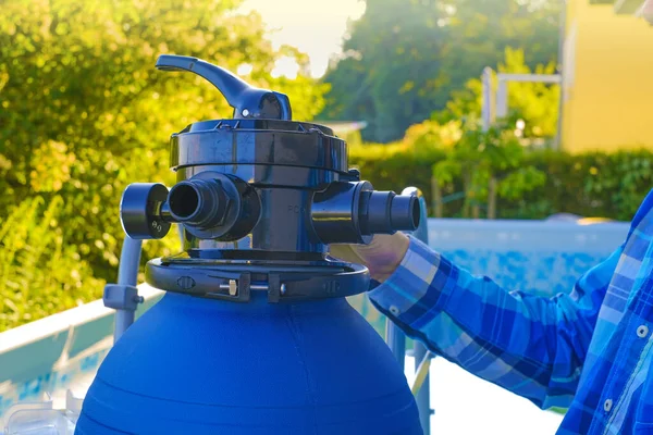 Swimming pool Filter.Swimming pool cleaning equipment. Blue water filter in the hands of a man in a plaid shirt . A man moves the hoses to the filter in the pool.