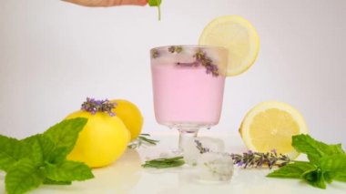 Lavanta kokteyli. Bir el kokteyl bardağına nane şekeri koyar. Lavantalı limon. Mor kokteyl, buz, limon ve lavanta çiçeği. Ferahlatıcı yaz kokteylleri, içkiler. yavaş çekim.