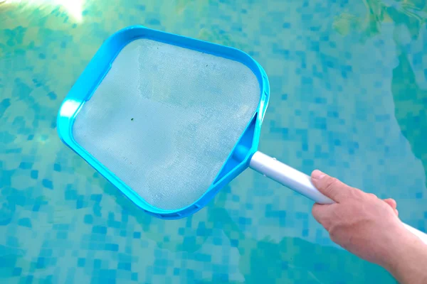 Swimming Pool Cleaning.Net for cleaning the pool in hands on blue water background.Filtration of water with a net in the pool.Pool cleaning tool