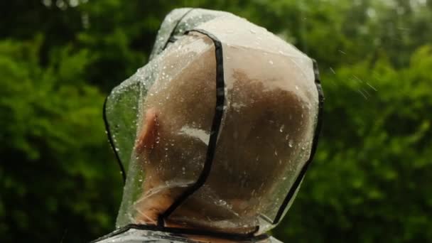 Βροχοποιός στη βροχή. Βροχή πέφτει στο καπό ενός αδιάβροχου. Ένας άντρας με διάφανο αδιάβροχο σε καλοκαιρινό κήπο.Βροχερός καιρός. — Αρχείο Βίντεο