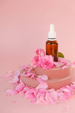 Cam bir şişede gül yağı ve pembe bir podyumda gül çiçeği. Doğal gül yağı. Aromaterapi ve kozmetik ürünleri. Organik kozmetik.