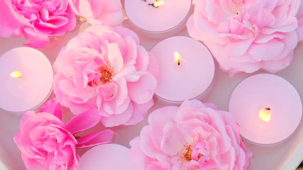 Κεριά με άρωμα τριαντάφυλλου.Κεριά αρωματοθεραπείας και spa Κεριά με άρωμα τριαντάφυλλου.Κεριά με άρωμα τριαντάφυλλου.Ροζ κεριά που καίνε και ροζ τριαντάφυλλα στο νερό. — Αρχείο Βίντεο