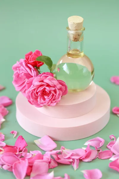 Rose olejek eteryczny w szklanej butelce w kwiatach róż na podium na zielonym tle.Aromaterapia i kosmetyki. naturalne olejki różowe.Kosmetyki ekologiczne — Zdjęcie stockowe