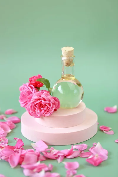 Rose olejek eteryczny w szklanej butelce w kwiatach róż na różowym podium na zielonym tle.Aromaterapia i kosmetyki. naturalne olejki różowe.Kosmetyki ekologiczne — Zdjęcie stockowe