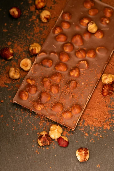 Schokoladenbar.Schokolade mit Haselnüssen und Kakaopulver auf Schiefergrund. Schokoladendessert mit Nüssen. Desserts und Süßigkeiten — Stockfoto