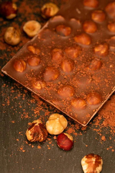Schokoladenbar.Schokolade mit Haselnüssen und Kakaopulver auf Schiefergrund. Schokoladendessert mit Nüssen. — Stockfoto