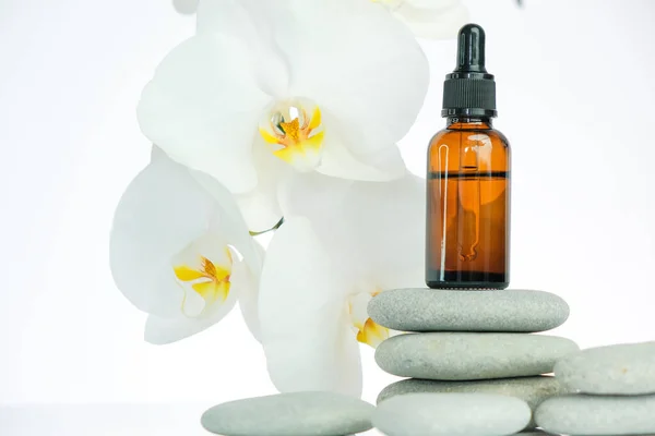 Aceite de masaje y piedras de masaje. botella de vidrio con aceite de masaje sobre piedras grises y flor de orquídea sobre fondo blanco.Spa y aromaterapia.. — Foto de Stock