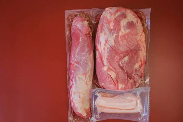 Stück Fleisch in einem Vakuum. Fleisch und Schweinefett in Vakuumbeuteln auf weinrotem Hintergrund. Proteinernährung. — Stockfoto