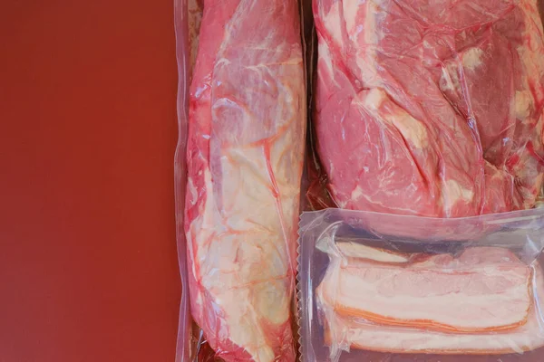 Carne in un aspirapolvere Carne e grasso di maiale in sacchetti sottovuoto su uno sfondo bordeaux. Alimentazione proteica. Fattoria carni fresche biologiche — Foto Stock