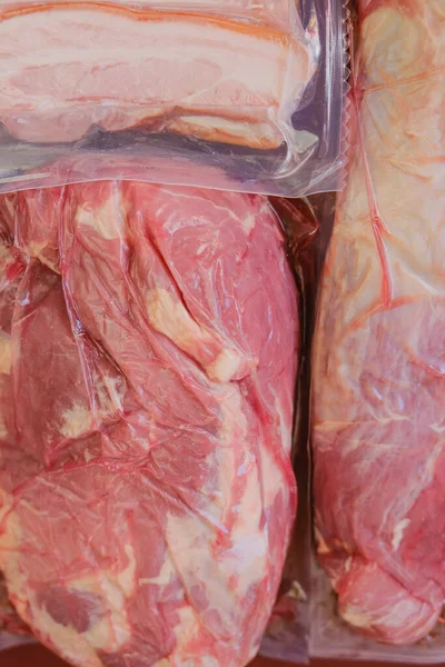 Produtos de carne. Carne e gordura de porco em sacos de vácuo. Nutrição proteica. Carne orgânica da fazenda em um fundo vermelho.Carne fresca crua — Fotografia de Stock