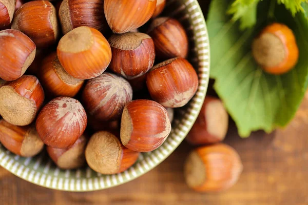 Las avellanas de cerca en una taza verde sobre una mesa de madera. Nueces enteras con hojas verdes. cosecha de avellanas. Avellanas orgánicas cultivadas. Grasas saludables.Avellanas harvest.view desde arriba. —  Fotos de Stock